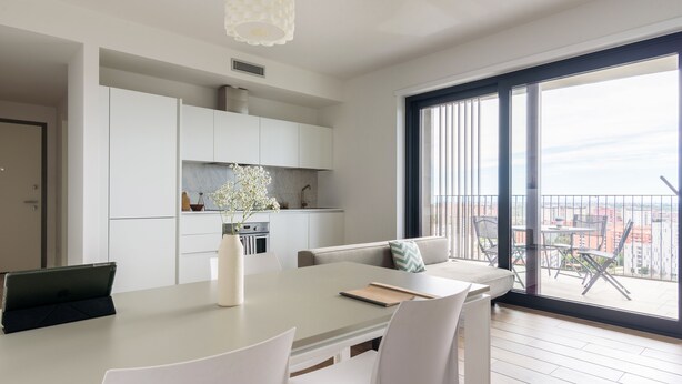 A modern kitchen with white cabinets, a dining area with a table and chairs, and a large window with a view of buildings.