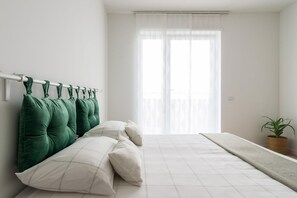 A bedroom with a bed, green and white pillows, a plant, and a window with sheer curtains. - JOIVY Uptown Apartments (Milan)
