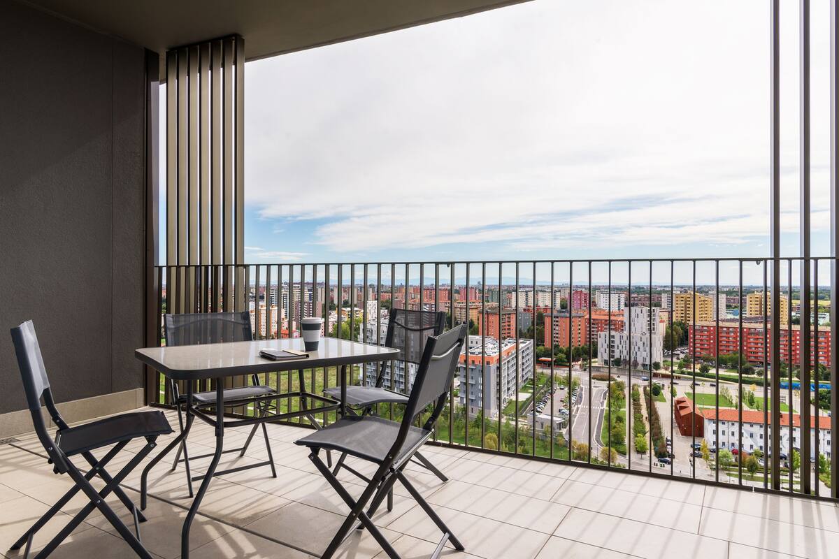 A balcony with a table and chairs, offering a view of a cityscape.