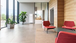 A modern waiting area with a large window, a potted plant, and red chairs.