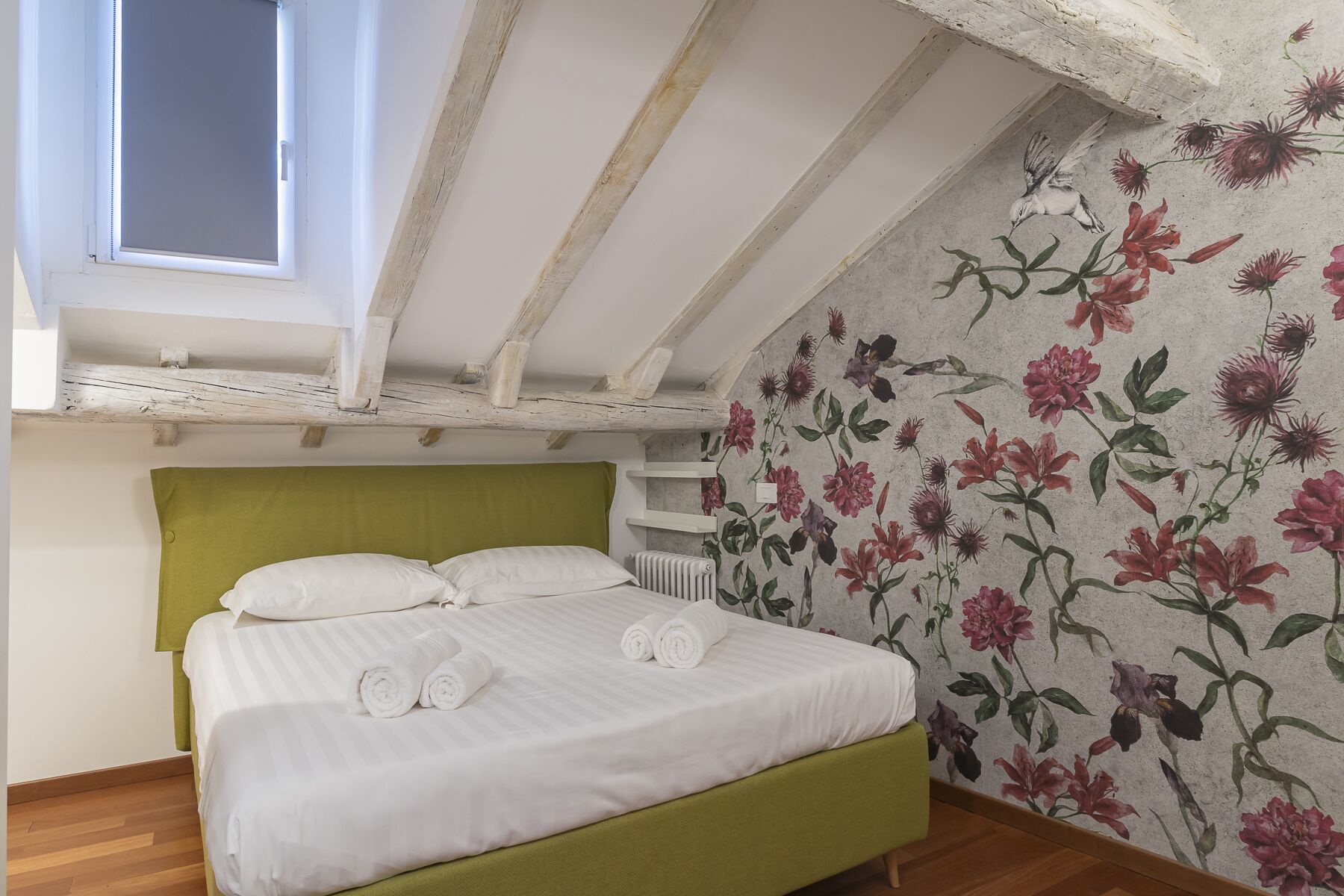 A bedroom with a green headboard, a bed with white linens, and a floral wallpaper.