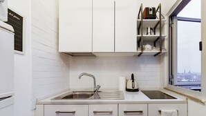 Une cuisine moderne avec des meubles blancs, un évier en acier inoxydable et une fenêtre donnant sur la ville.