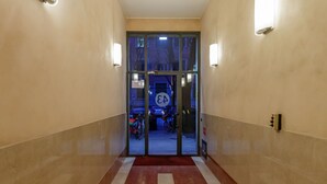 Un couloir recouvert d’une moquette rouge menant à une entrée avec une porte en verre.