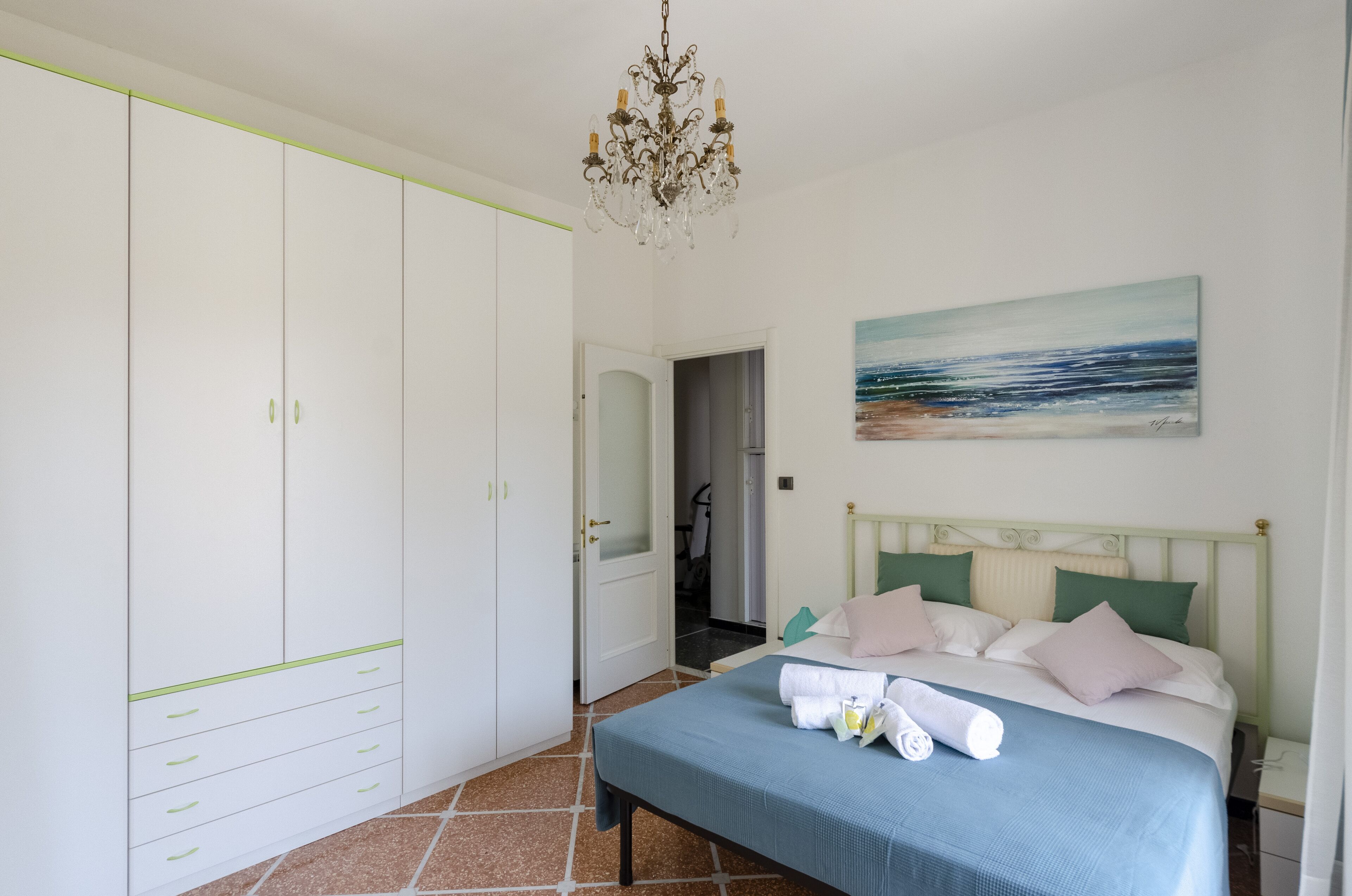 A bedroom with a bed, a wardrobe, a painting, and a chandelier.