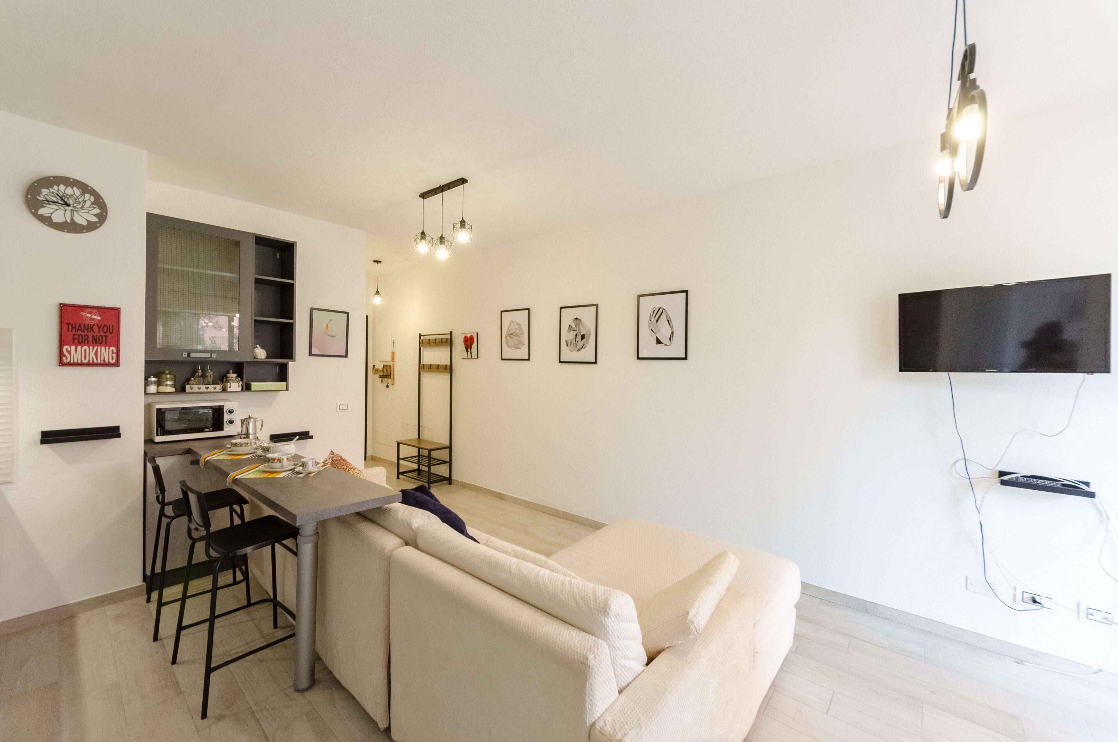 Una sala de estar moderna con un sofá, una zona de comedor con sillas, una cocina con microondas y un televisor montado en la pared.
