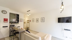 A modern living room with a sofa, a dining area with chairs, a kitchen area with a microwave, and a TV mounted on the wall. - JOIVY Flat W/Terrace & Parking (Sestri Levante)
