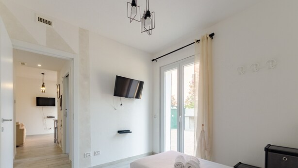A modern hotel room with two beds, a flat-screen TV, a large window with curtains, and a view of the outside. - JOIVY Flat W/Terrace & Parking (Sestri Levante)