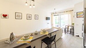 A modern kitchen with a long island, bar stools, and a dining area. There are framed artworks on the walls and a window with curtains. - JOIVY Flat W/Terrace & Parking (Sestri Levante)