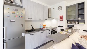 A compact kitchen with a refrigerator, stove, sink, and a dining area with a table and chairs. - JOIVY Flat W/Terrace & Parking (Sestri Levante)
