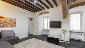 A modern living room with a grey sofa, a white shag rug, a flat-screen TV, and a standing fan. - JOIVY Flat In Perfect Centre (Genoa)