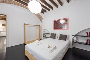 Quarto moderno com cama de madeira, roupa de cama branca, guarda-roupa de madeira, mesa de cabeceira com abajur e estante de livros.