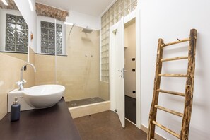 Une salle de bain avec un lavabo blanc, une douche et une échelle en bois appuyée contre le mur.
