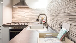 A modern kitchen with a gas stove, stainless steel sink, and a wooden backsplash. - JOIVY Flat In Perfect Centre (Genoa)