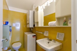 A bathroom with yellow tiles, a white toilet, a sink with a mirror above it, and a small heater on the floor. - JOIVY Flat W/Terrace & Sea View (Zoagli)