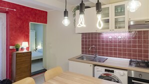 Eine kompakte Küche mit Spüle, Herd und Waschmaschine, ein Essbereich mit Tisch und Stühlen sowie eine Wand in Rot als Akzent.