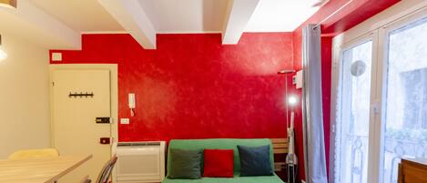 A room with a green bed, red walls, a white door, and a window with a view.
