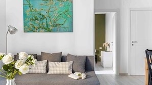 A modern living room with a grey sofa, a white vase with flowers, and a painting of a tree. - JOIVY Cosy 1-Bed Flat In Navigli (Milan)
