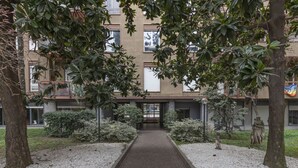 Polku johtaa modernia arkkitehtuuria edustavaan rakennukseen, jonka ympärillä on puita ja huoliteltua puutarhaa.