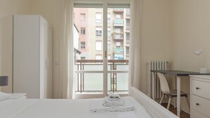 Hotellihuone, jossa on sänky, työpöytä, tuoli, patteri ja suuret ikkunat, joista avautuu näkymä kaupunkiin.