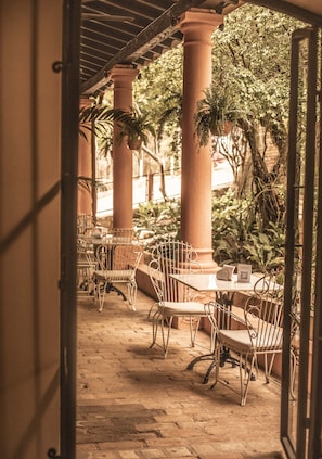An outdoor patio area with tables and chairs, surrounded by columns and potted plants.