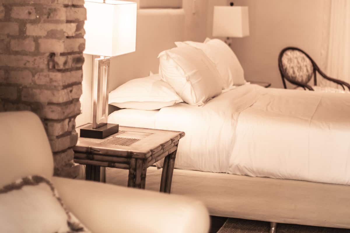 Une chambre d’hôtel avec un mur en briques, un lit avec une literie blanche, une table de chevet avec une lampe et une chaise.