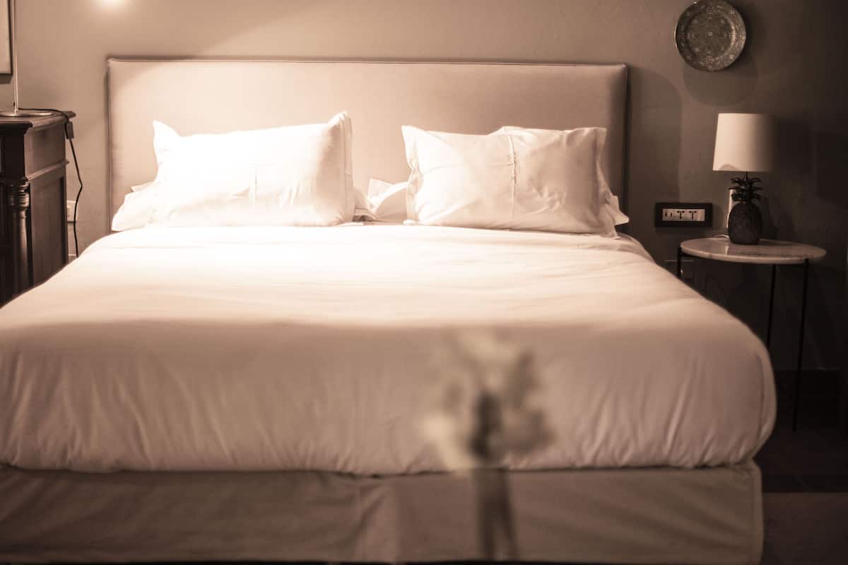 Un lit bien fait, avec du linge de lit blanc, dans une chambre d’hôtel.