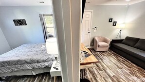 Ett rum med en säng, ett litet bord, en stol, en soffa och en lampa.