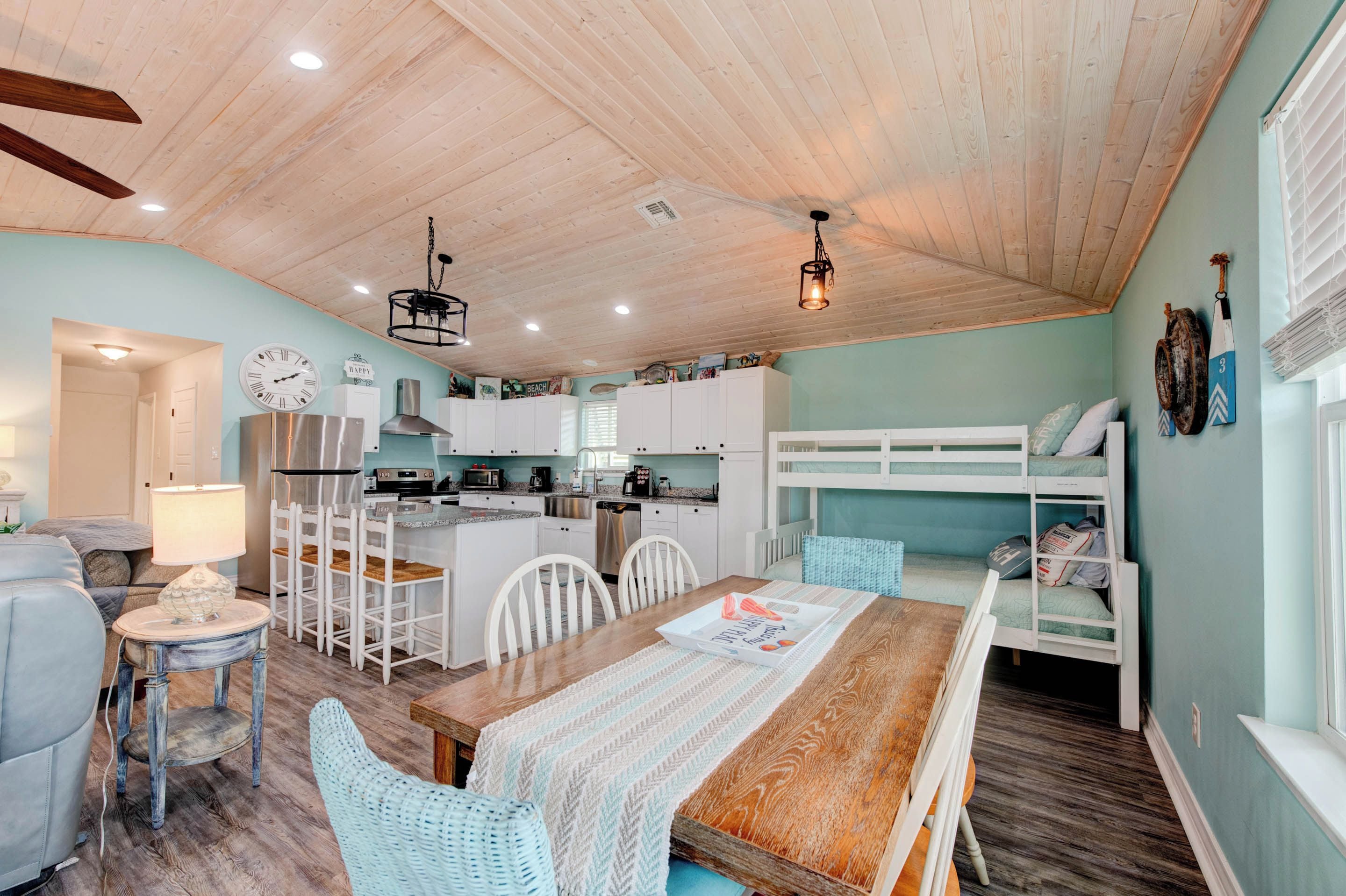 A cozy, well-lit room with a wooden ceiling, a dining table with chairs, a bunk bed, and a kitchenette.