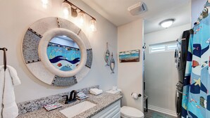 A bathroom with a round mirror, a sink, a toilet, and a shower area. - A- Rocks Resort by Silver Sands Vacation Rentals (Port Aransas)