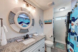 A bathroom with a round mirror, a sink, a toilet, and a shower area. - A- Rocks Resort by Silver Sands Vacation Rentals (Port Aransas)