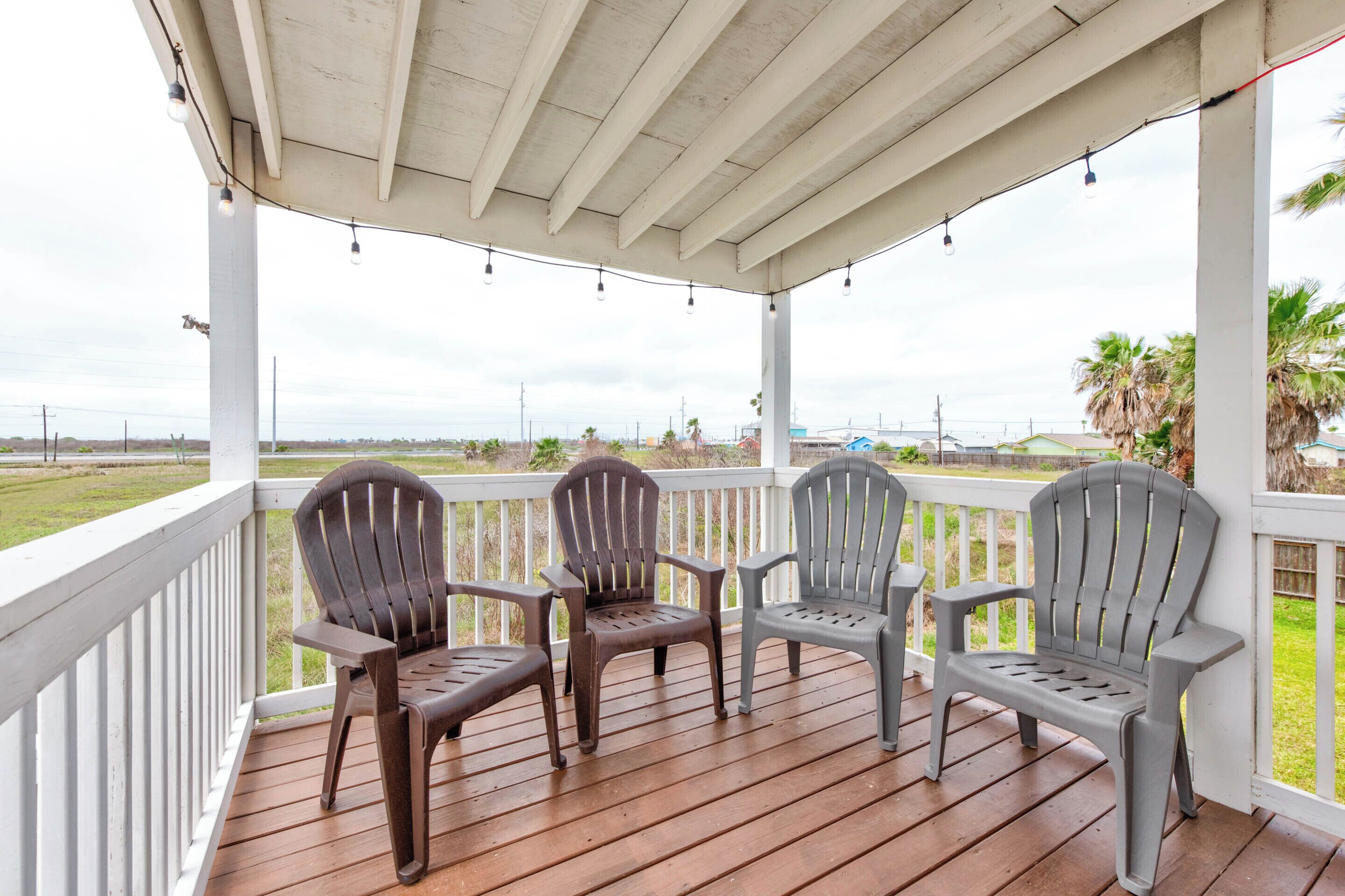 Eine überdachte Veranda mit Holzboden und weißen Geländern, ausgestattet mit drei Adirondack-Stühlen und Lichterketten.