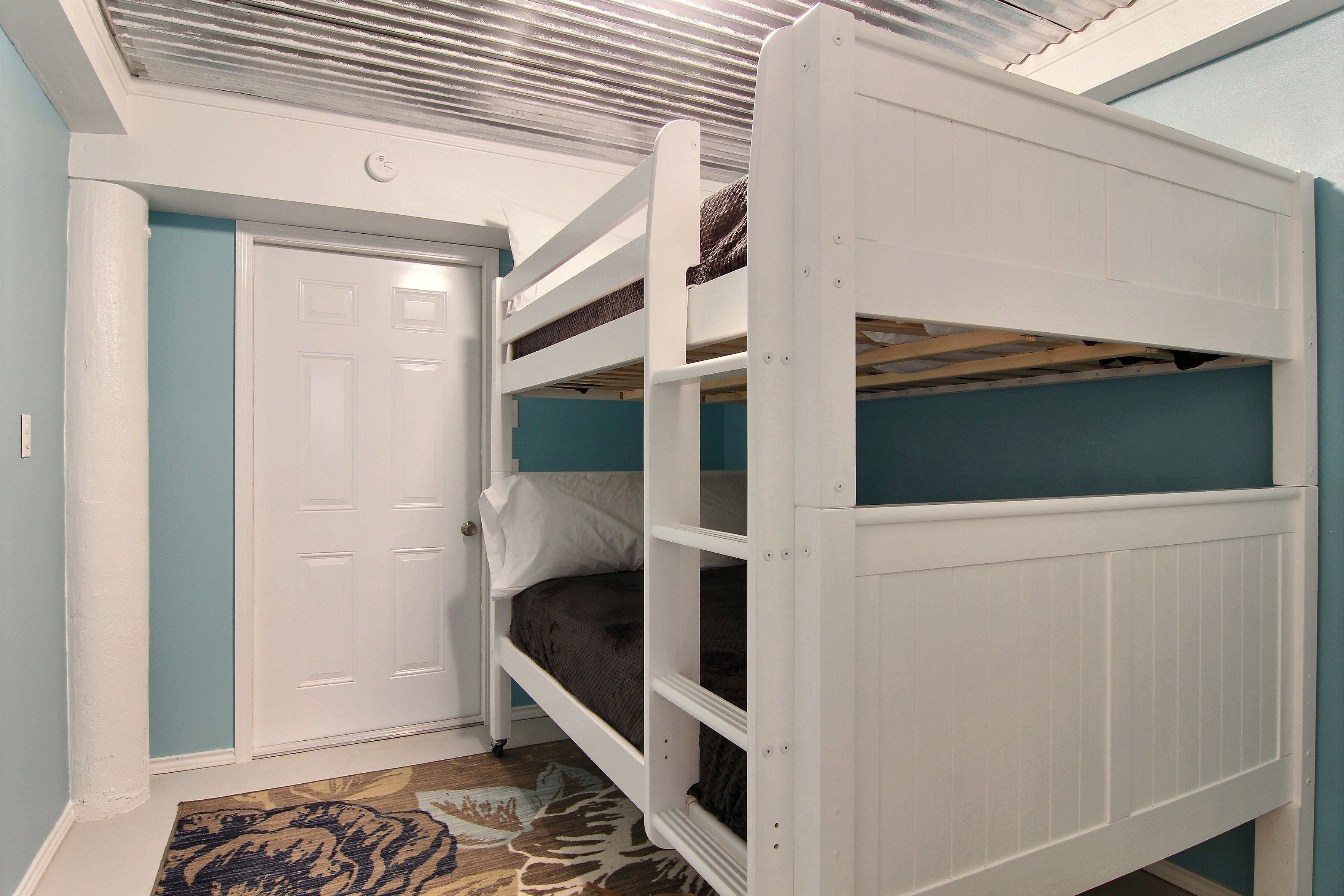 A bunk bed with a white frame and a blue wall.