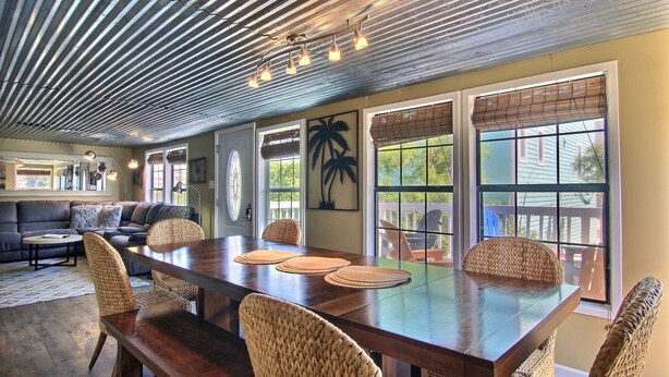 A spacious dining area with a long wooden table, wicker chairs, and large windows with blinds. - 4 Palms by Silver Sands Vacation Rentals (Port Aransas)