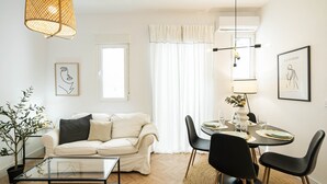Un salon moderne avec un canapé, une table basse et un coin repas comprenant des chaises et une table dressée pour deux personnes.