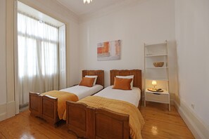 Een kamer met twee houten bedden, een nachtkastje met een lamp, een plank met een schaal, en een schilderij aan de muur.