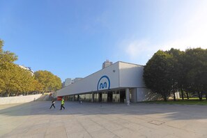 Een modern gebouw met een groot logo op de gevel, een ruim entreegebied en een heldere lucht.