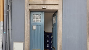Eine blaue Tür mit Nummernschild, einem kleinen Stromkasten und einer mit geometrischen Mustern versehenen Fliesenwand.