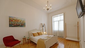 Ein Schlafzimmer mit einem Bett, einem roten Sessel, einem Gemälde, einer Chandelüster und einem Fernseher.