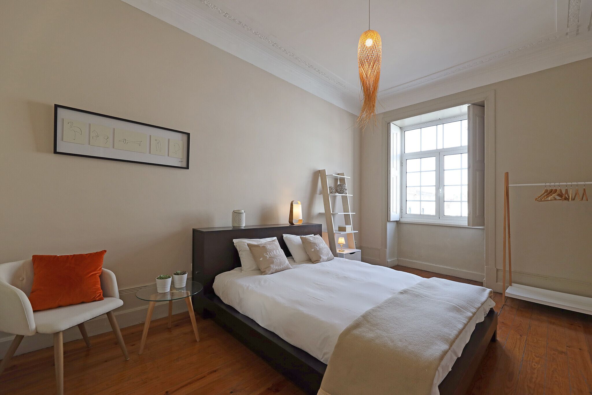 Une chambre à coucher comprenant un lit, une chaise, une petite table, une fenêtre et une étagère fixée au mur.