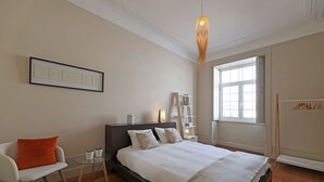 Una camera da letto con un letto, una sedia, un tavolino, una finestra e una mensola a parete.