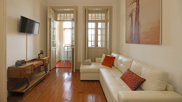 Un soggiorno con un divano bianco, un tavolino in legno, una televisione a schermo piatto e un quadro appeso al muro.