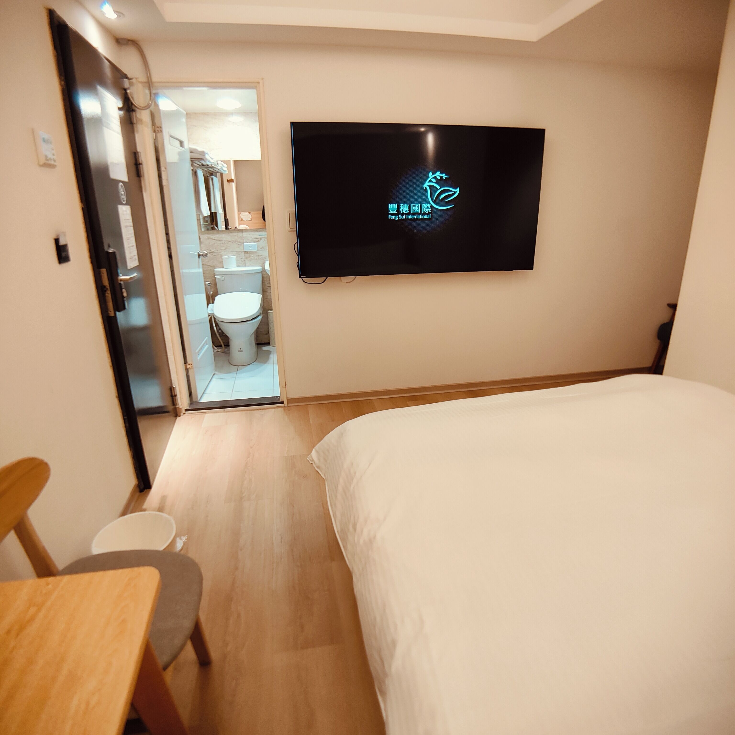 Habitación de hotel con cama, escritorio, silla, inodoro y televisor montado en la pared.