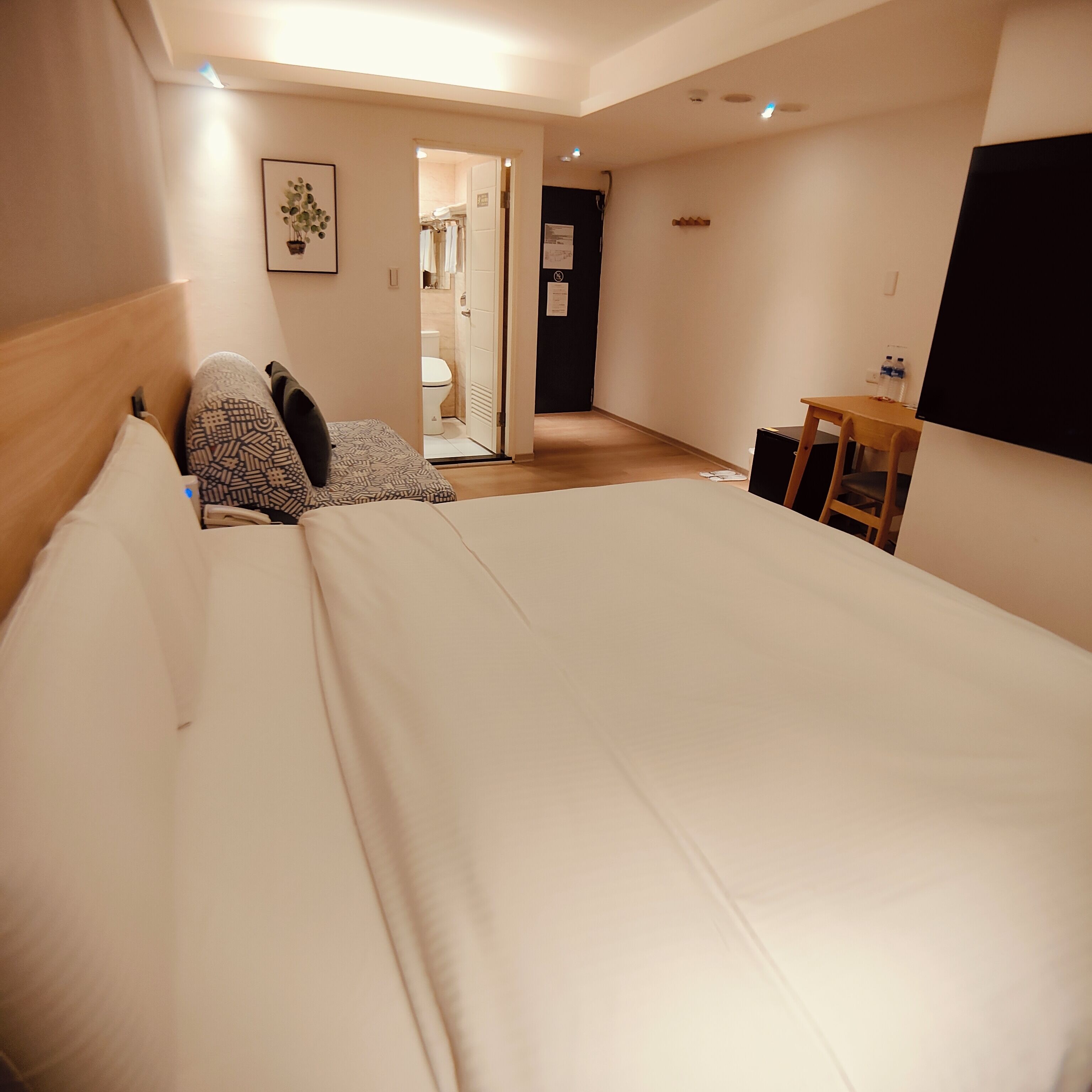 A bedroom with a large bed, a wooden headboard, a bedside table with a lamp, and a door leading to a bathroom.
