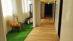 A hotel corridor with wooden flooring, a green carpeted area, and a massage chair. - FooYee Hotel-YongHe (New Taipei City)
