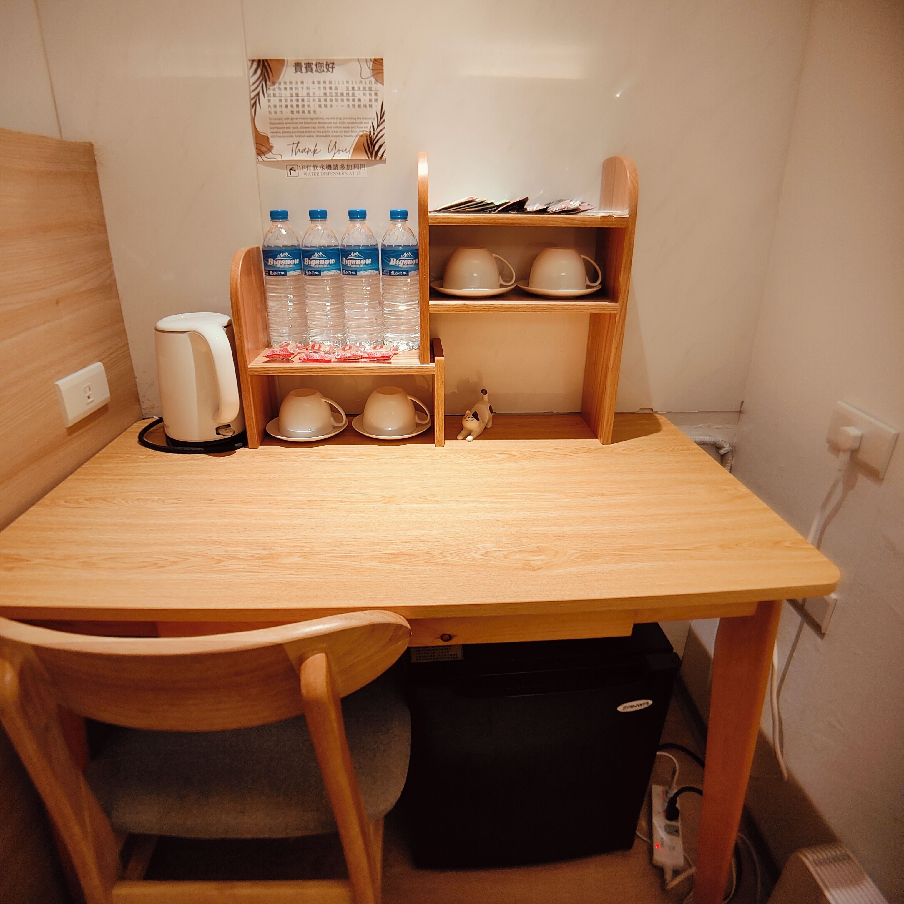 A small wooden table with a kettle, water bottles, and cups on shelves.