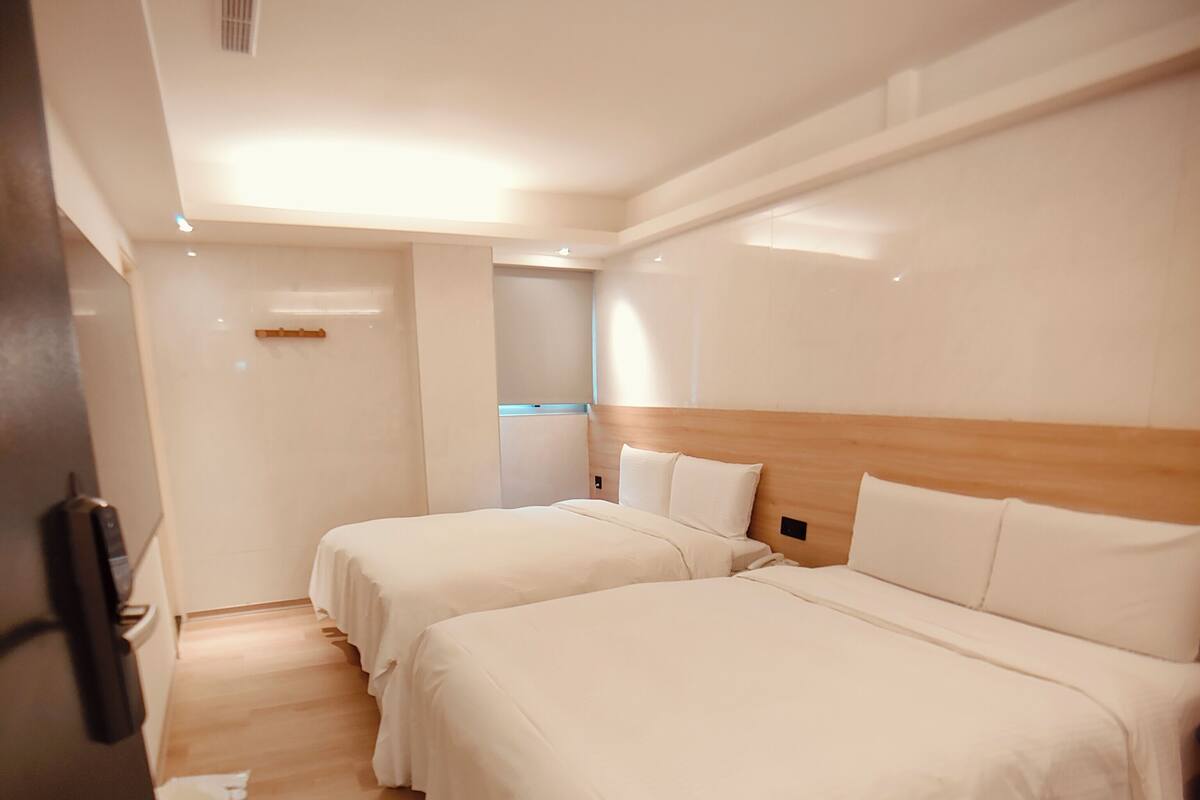 A hotel room with two beds, wooden flooring, and white walls.
