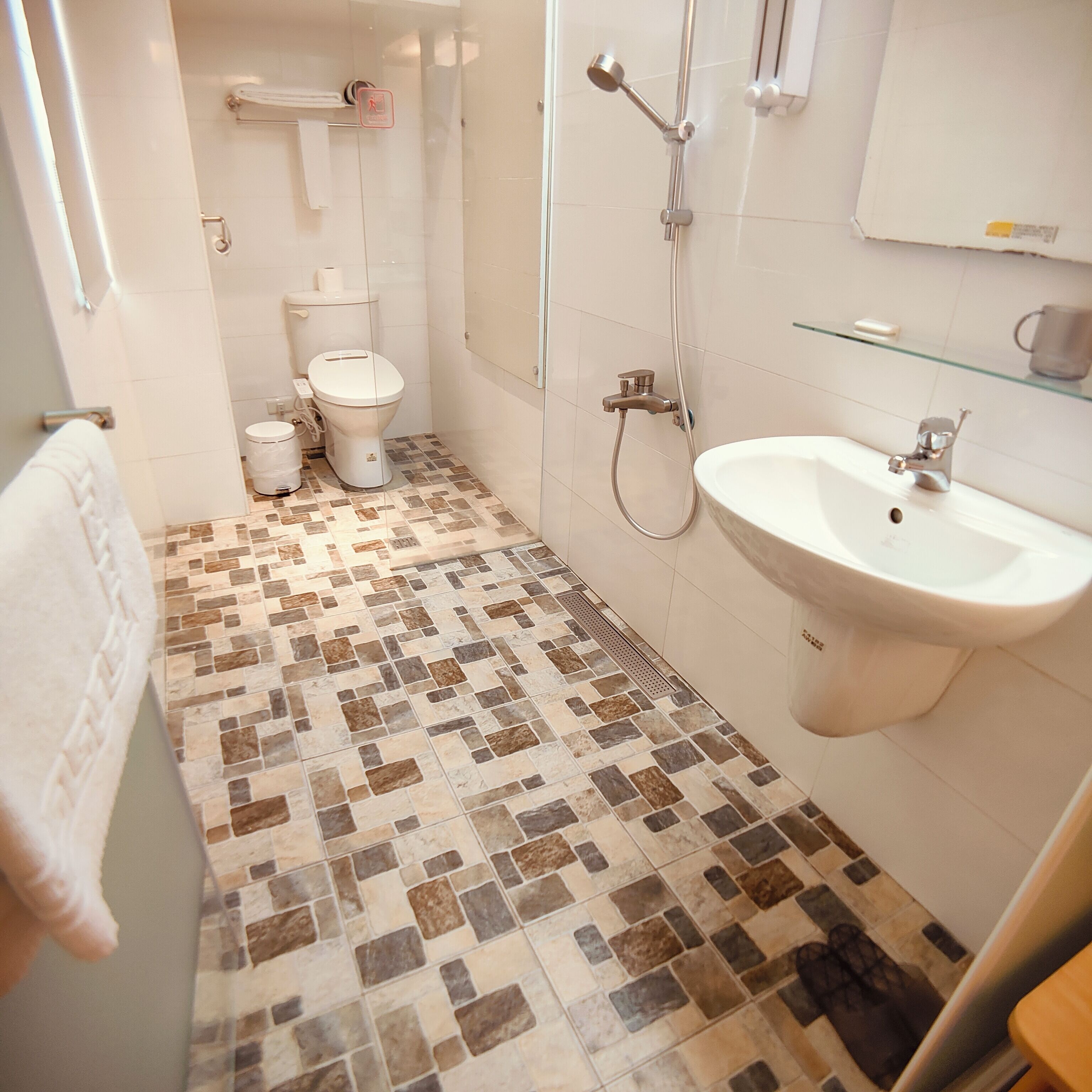Et badeværelse med flisegulv, håndvask, toilet og brusebad.