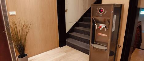 A hallway with a refrigerator, a potted plant, and a staircase.