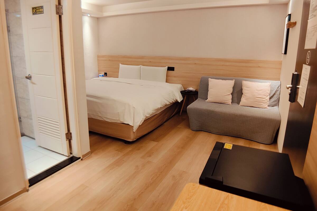 A hotel room with a bed, a sofa, a small table, and a door leading to a bathroom.