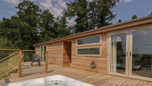 A wooden deck with a hot tub, a covered seating area, and a glass door leading to a covered patio.